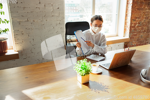 Image of Woman working in office alone during coronavirus or COVID-19 quarantine, wearing face mask