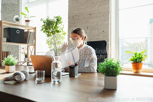 Image of Woman working in office alone during coronavirus or COVID-19 quarantine, wearing face mask