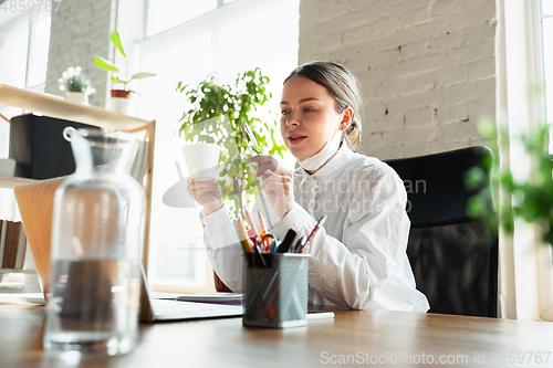 Image of Woman working in office alone during coronavirus or COVID-19 quarantine, wearing face mask