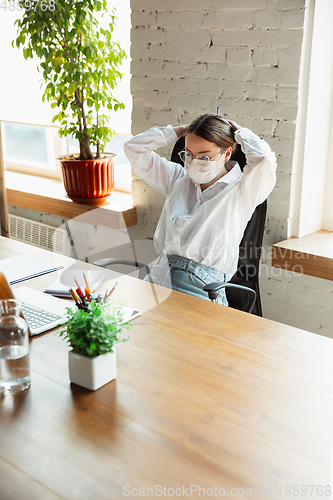 Image of Woman working in office alone during coronavirus or COVID-19 quarantine, wearing face mask