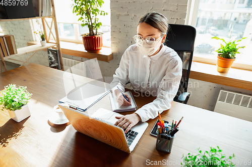 Image of Woman working in office alone during coronavirus or COVID-19 quarantine, wearing face mask