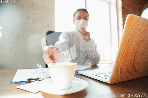 Image of Woman working in office alone during coronavirus or COVID-19 quarantine, wearing face mask