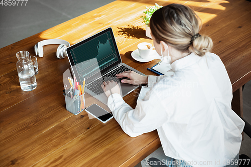 Image of Woman working in office alone during coronavirus or COVID-19 quarantine, wearing face mask