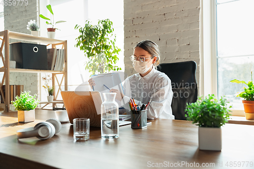 Image of Woman working in office alone during coronavirus or COVID-19 quarantine, wearing face mask