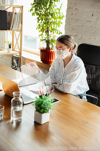 Image of Woman working in office alone during coronavirus or COVID-19 quarantine, wearing face mask