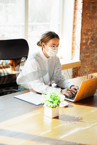 Image of Woman working in office alone during coronavirus or COVID-19 quarantine, wearing face mask