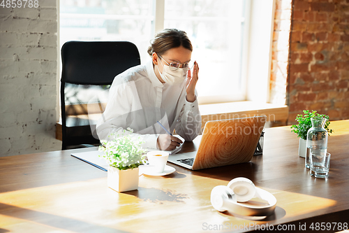 Image of Woman working in office alone during coronavirus or COVID-19 quarantine, wearing face mask