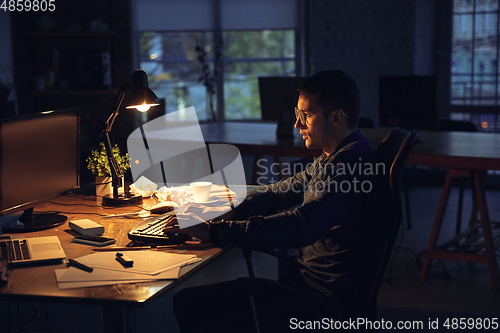 Image of Man working in office alone during coronavirus or COVID-19 quarantine, staying to late night