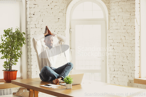 Image of Young african-american man doing yoga at home while being quarantine and freelance working