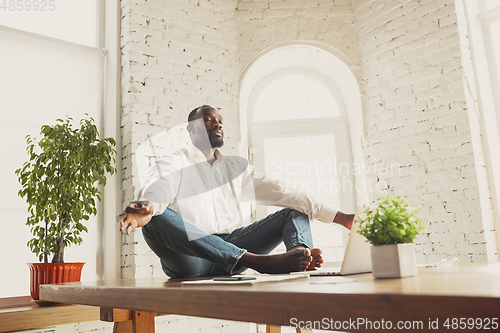 Image of Young african-american man doing yoga at home while being quarantine and freelance working