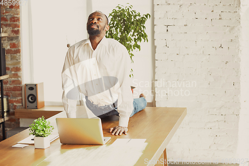 Image of Young african-american man doing yoga at home while being quarantine and freelance working