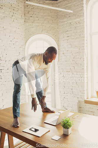 Image of Young african-american man doing yoga at home while being quarantine and freelance working