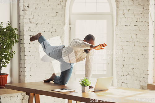 Image of Young african-american man doing yoga at home while being quarantine and freelance working