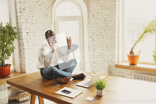 Image of Young african-american man doing yoga at home while being quarantine and freelance working