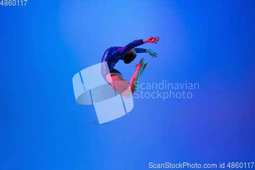 Image of Young flexible girl isolated on blue studio background. Young female model practicing artistic gymnastics. Exercises for flexibility, balance.