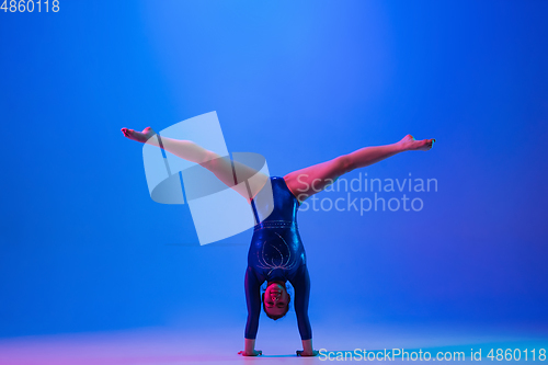 Image of Young flexible girl isolated on blue studio background. Young female model practicing artistic gymnastics. Exercises for flexibility, balance.