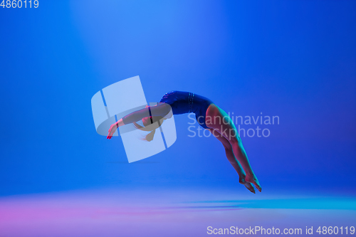 Image of Young flexible girl isolated on blue studio background. Young female model practicing artistic gymnastics. Exercises for flexibility, balance.
