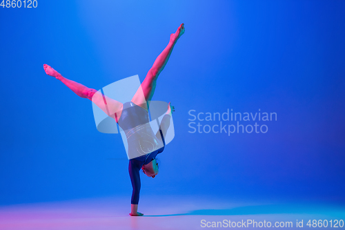 Image of Young flexible girl isolated on blue studio background. Young female model practicing artistic gymnastics. Exercises for flexibility, balance.