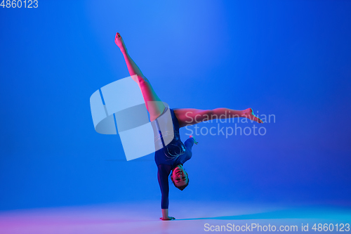 Image of Young flexible girl isolated on blue studio background. Young female model practicing artistic gymnastics. Exercises for flexibility, balance.