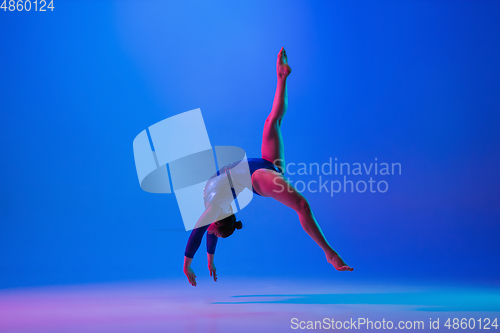 Image of Young flexible girl isolated on blue studio background. Young female model practicing artistic gymnastics. Exercises for flexibility, balance.