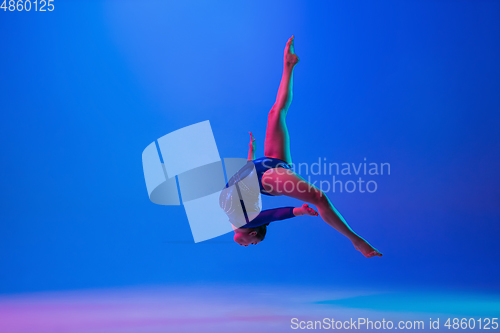 Image of Young flexible girl isolated on blue studio background. Young female model practicing artistic gymnastics. Exercises for flexibility, balance.