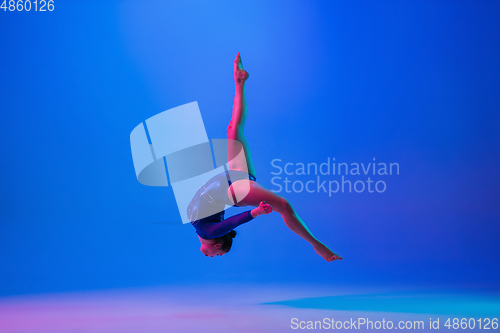 Image of Young flexible girl isolated on blue studio background. Young female model practicing artistic gymnastics. Exercises for flexibility, balance.