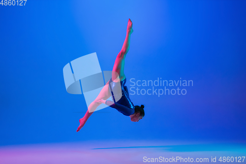 Image of Young flexible girl isolated on blue studio background. Young female model practicing artistic gymnastics. Exercises for flexibility, balance.