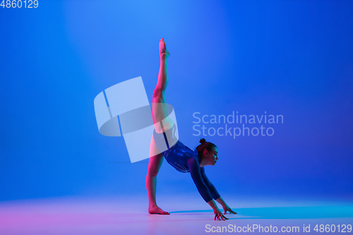 Image of Young flexible girl isolated on blue studio background. Young female model practicing artistic gymnastics. Exercises for flexibility, balance.