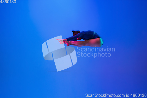 Image of Young flexible girl isolated on blue studio background. Young female model practicing artistic gymnastics. Exercises for flexibility, balance.