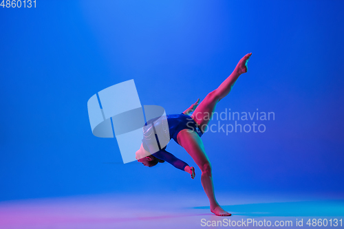 Image of Young flexible girl isolated on blue studio background. Young female model practicing artistic gymnastics. Exercises for flexibility, balance.