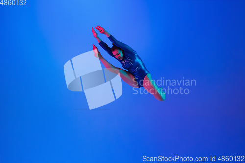 Image of Young flexible girl isolated on blue studio background. Young female model practicing artistic gymnastics. Exercises for flexibility, balance.