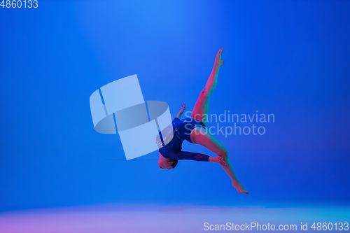 Image of Young flexible girl isolated on blue studio background. Young female model practicing artistic gymnastics. Exercises for flexibility, balance.