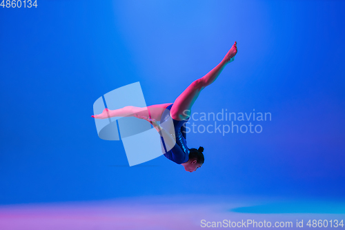 Image of Young flexible girl isolated on blue studio background. Young female model practicing artistic gymnastics. Exercises for flexibility, balance.