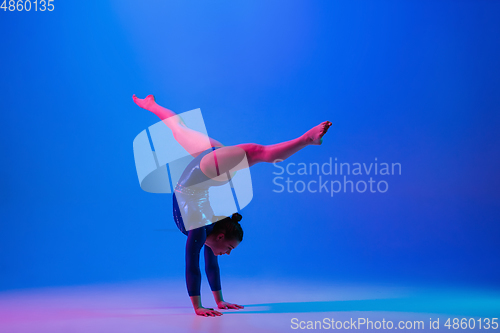 Image of Young flexible girl isolated on blue studio background. Young female model practicing artistic gymnastics. Exercises for flexibility, balance.