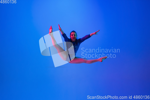 Image of Young flexible girl isolated on blue studio background. Young female model practicing artistic gymnastics. Exercises for flexibility, balance.