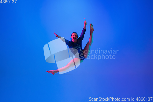 Image of Young flexible girl isolated on blue studio background. Young female model practicing artistic gymnastics. Exercises for flexibility, balance.