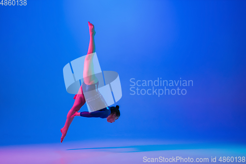 Image of Young flexible girl isolated on blue studio background. Young female model practicing artistic gymnastics. Exercises for flexibility, balance.