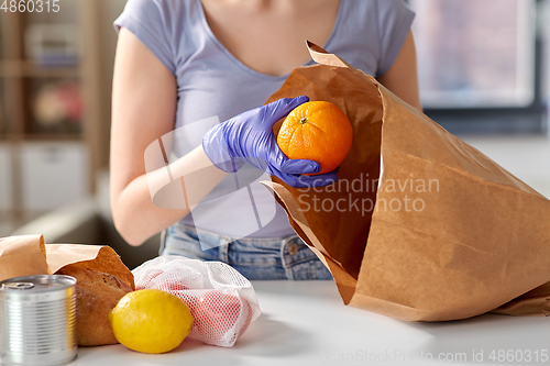 Image of woman in gloves taking food from paper bag at home