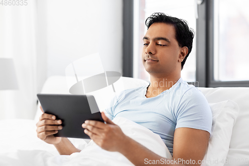 Image of happy indian man with tablet pc in bed at home