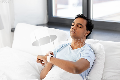 Image of happy indian man with smart watch in bed at home