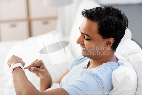 Image of happy indian man with smart watch in bed at home