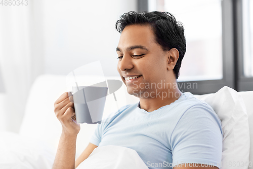 Image of happy indian man drinking coffee in bed at home