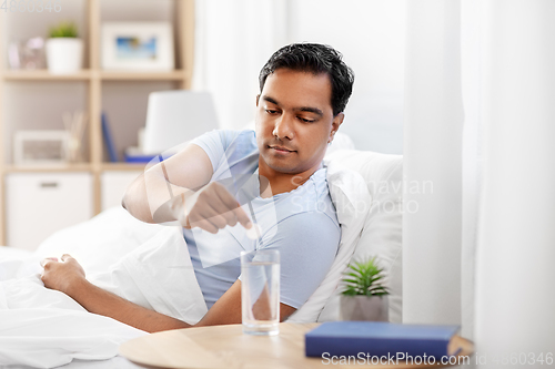 Image of man in bed dropping medicine into glass of water