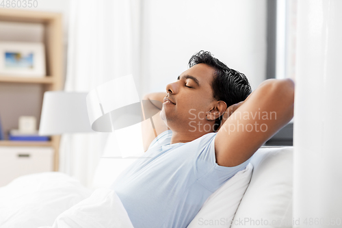 Image of indian man stretching in bed at home