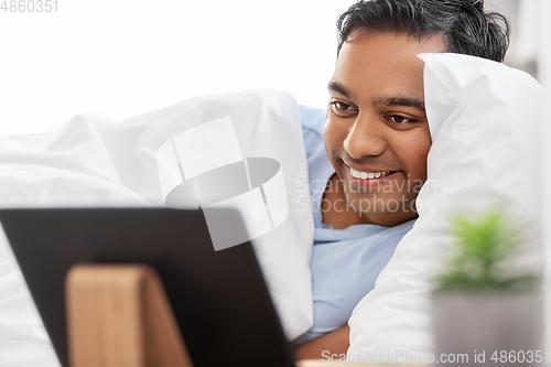 Image of happy indian man with tablet pc in bed at home