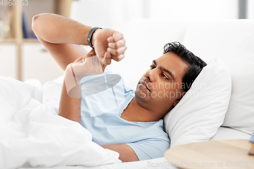 Image of indian man with health tracker in bed at home