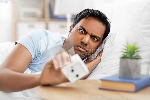 Image of overslept indian man in bed looking at alarm clock