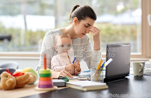 Image of tired mother with baby working at home office