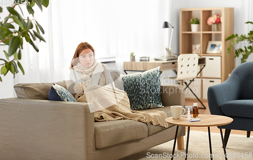 Image of sad sick woman in blanket and scarf at home