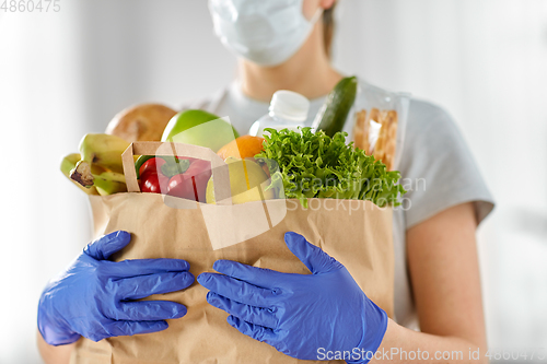 Image of woman in gloves with food in paper bag at home